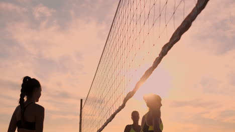 Gruppe-Junger-Mädchen,-Die-Beachvolleyball-Bei-Sonnenuntergang-Oder-Sonnenaufgang-In-Zeitlupe-Spielen.-Schöne-Mädchen-Im-Bikini-Spielen-Professionell-Volleyball-Auf-Dem-Sand